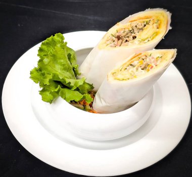 İki doğranmış et, karışık sebze, marul ve kremalı sos taze yeşilliklerle birlikte beyaz bir kasede dikey olarak sunuluyor..