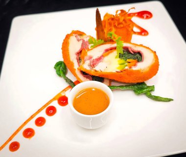 Peynir ve ıspanak dolgusunu ortaya çıkarmak için dilimlenmiş içi doldurulmuş tavuk dolması, kavrulmuş domates ve beyaz bir tabakta portakal sosu kabı ile servis edilir..