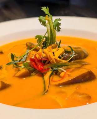 Patlıcanlı karides, bambu filizleri, kırmızı biber ve hindistan cevizi sütü, kişniş ve canlı kontrastlar için yenilebilir çiçeklerle süslenmiş.