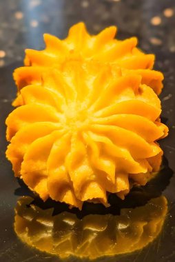 Bir yığın altın esmer tereyağlı kurabiye, kabarık, çiçeğe benzer şekilli, borulu ve çıtır çıtır bir dokuya pişirilmiş. Koyu renkli yansıtıcı yüzeyde dikey şekillendirilmiş, sıcak ışıklandırmalı, fırın menüleri için ideal..