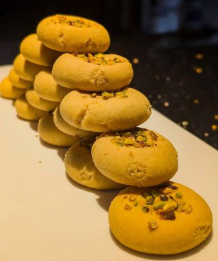 Beyaz dikdörtgen bir tabağa istiflenmiş fıstık ezmeli kurabiyeler ve açık altın parçacıklı bir doku..