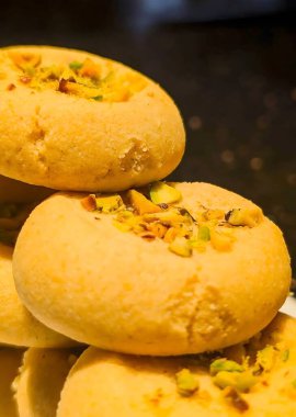 Beyaz dikdörtgen bir tabağa istiflenmiş fıstık ezmeli kurabiyeler ve açık altın parçacıklı bir doku..