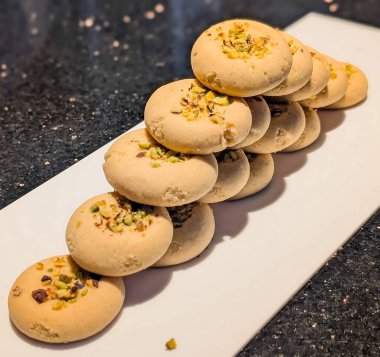 Beyaz dikdörtgen bir tabağa istiflenmiş fıstık ezmeli kurabiyeler ve açık altın parçacıklı bir doku..