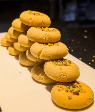 Beyaz dikdörtgen bir tabağa istiflenmiş fıstık ezmeli kurabiyeler ve açık altın parçacıklı bir doku..