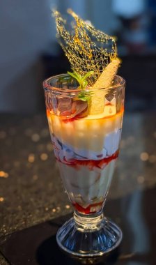 Kremalı vanilyalı krema katılmış gurme çilekli parfe, meyve ezmesi ve kek parçaları, üzerinde gofret çubuğu, nane ve altın şekerli tüy..