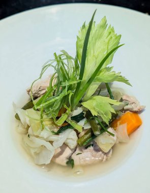 Temiz tavuk ve sebze çorbası havuç, lahana, yeşil fasulye ve taze otlar taze tavuk parçaları ve taze baharatlı et suyuyla birlikte beyaz bir tabakta servis edilir..