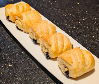 Koyu çikolata dolgulu acı au chocolat hamur işleri ve tereyağlı puf börekleri dikdörtgen beyaz servis tabağında düzgün bir sıraya dizilir..