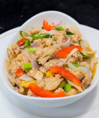 Çan biberi, soğan ve yeşil soğanlı rengarenk tavuk kızartması. Parlak, lezzetli bir sosla servis ediliyor. Aynı tabakta beyaz bir kasede servis ediliyor..