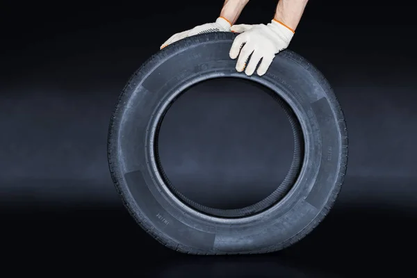 Man presses on new tire on creative black background. Tire changing concept