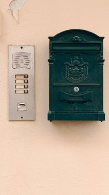 İtalya 'da bej bir sıva duvarında metal bir dahili telefon panelinin yanında kabartmalı arması olan koyu yeşil bir posta kutusu..