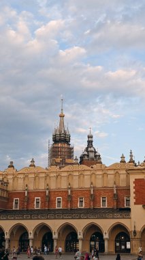 Günbatımında Krakow 'un Ana Pazar Meydanı' ndaki St. Mary Bazilikası 'nın gotik kuleleri olan tarihi Kulis Binası' nda insanlar aşağıda yürüyor.