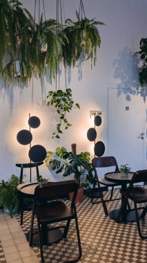 Modern siyah sandalyeleri ve mozaik döşemeleri olan şık kapalı kafe köşeleri, yemyeşil bitkiler ve dramatik duvar ışıklarıyla çevrili, rahat, botanik esinlenilmiş bir ortam yaratıyor..