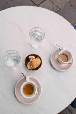 İki espresso bardağı, bir bardak su ve küçük bir kase kurabiye ile minimalist kafe masası. Sıcak kahve molası, yaşam tarzı, yiyecek ve içecek konsepti..
