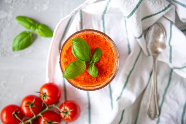 Beyaz arka planda soğuk domates çorbası, üst manzara. Geleneksel İspanyol çorbası. Küçük kiraz domatesleri, fesleğen yaprakları ve mutfak havlusu.. 
