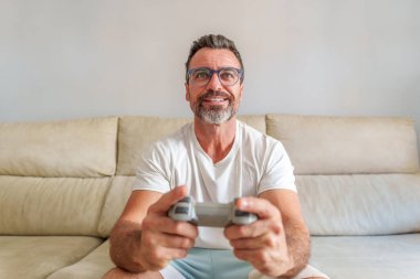 Evdeki kanepede video oyunları oynarken gülümseyen orta yaşlı adamın ön görünümü