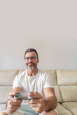 Evdeki kanepede video oyunları oynarken gülümseyen orta yaşlı adamın ön görünümü