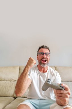 Ev Sahipleri 'ndeki koltukta video oyunları oynarken Zaferi Kutlayan Orta Yaşlı Adam' ın Ön Görünümü