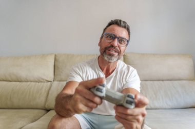 Evdeki kanepede video oyunları oynarken gülümseyen orta yaşlı adamın ön görünümü