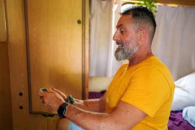 Orta yaşlı bir adam, karavanının içinde dinlenirken akıllı telefonuyla video oyunlarından hoşlanıyor.