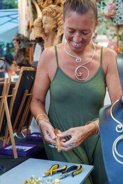 50 'li yaşlarda İspanyol bir kadın, Stall Stall' da el yapımı alüminyum mücevher satan küpeler yapıyor.