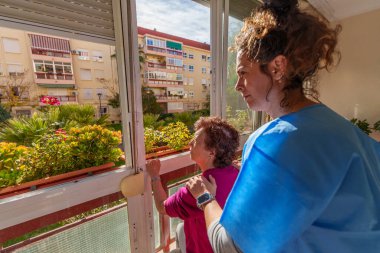 Güneşli bir günde pencereden dışarı bakan, huzurlu bir ortamda bakım ve bağlantı anlarını paylaşan yaşlı bir kadını rahatlatan hemşire.