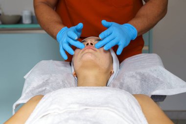Profesyonel güzellik uzmanı koruyucu mavi eldivenler giyip ultrasonik deri tedavisinden önce yüz masajı yapıyor.