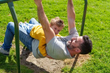 Baba ve oğul neşeli bir oyun parkında, neşeli bir günde güneşin tadını çıkarıyorlar.