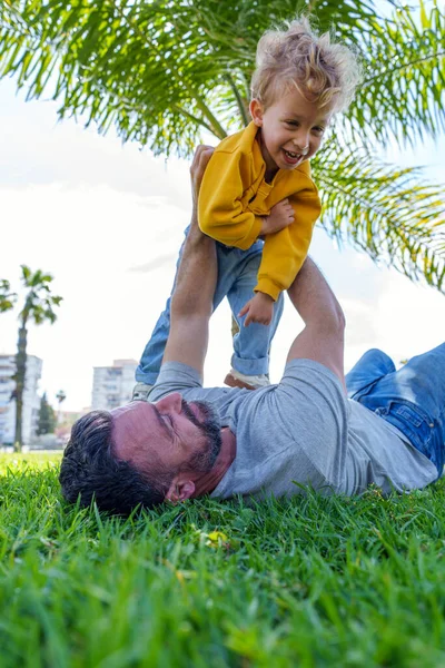 Baba çimenlerin üzerinde yatar, neşeli bir şekilde gülen oğlunu, sallanan bir palmiye ağacının altında, neşeyle kaldırır, aile birlikteliğimizi kutlar.