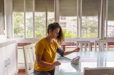 Endişeli Orta yaşlı kadın. Oturma odasında kan basıncını ölçüyor.