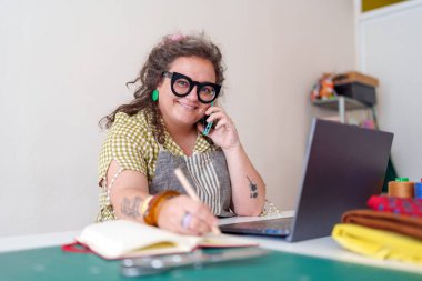 Küçük işletme atölyesinde çalışırken kadın girişimci emirleri yönetir, notlar yazar, telefonla konuşur.