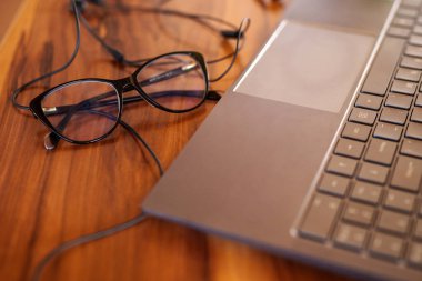 Modern dizüstü bilgisayarın yanında kablosuz kulaklıkların yanında duran siyah gözlükler kırsal ahşap çalışma alanı yüzeyinde verimliliği gösteriyor.