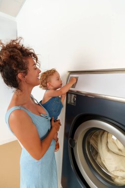Bebek, çamaşır makinesinin deliğine bozuk para sokuyor. İspanyol kadın çalıştırmak için çamaşır makinesine para atıyor. self-servis çamaşır fabrikası. 