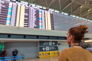 Havaalanında uçağını beklerken gelen ve giden yolcuların zaman çizelgesine bakıyor.