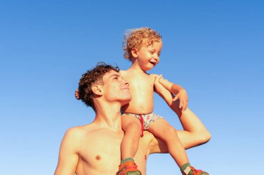 Genç adam kumsalda açık mavi gökyüzüne karşı yürümeye başladı.