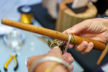 Ahşap bir aletle alüminyum kabloyu ustalıkla şekillendirerek, özenle el yapımı eşsiz mücevherler üreterek ellerini kapat.