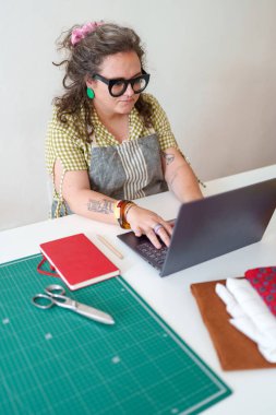 Dizüstü bilgisayar kullanan, siparişleri yöneten ve onun küçük iş yerindeki online mağazasında çalışan bir terzi.