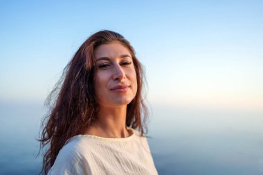 Huzurlu bir özgürlük deneyimi yaşayan, altın gün batımı ışığı altında okyanus ufkunun yanında duran, barışçıl bir duygu yayan sakin bir kadın modeli.