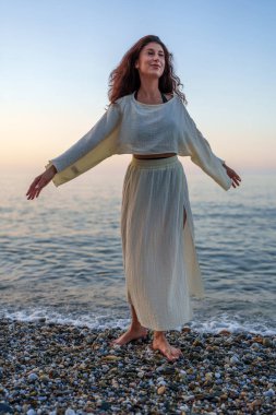Huzurlu kadın kollarını ardına kadar açıyor, altın gün batımında okyanus ufkuna bakıyor, kumlu kıyılarda huzur ve özgürlüğün vücut bulmuş hali.