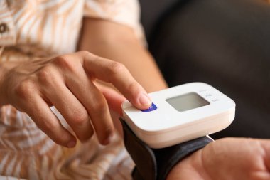 Bileğinde taşınabilir tansiyon monitörü olan bir kadının sağlık durumunu kontrol etmek için başlama düğmesine basılı görüntüsünü kapatın.