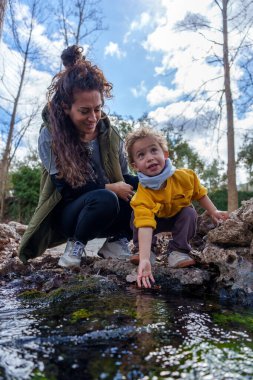 Derede suya dokunan meraklı çocuk, bereketli ormanda güneşli bir günün tadını çıkarırken annesinin yanında doğayı keşfediyor.