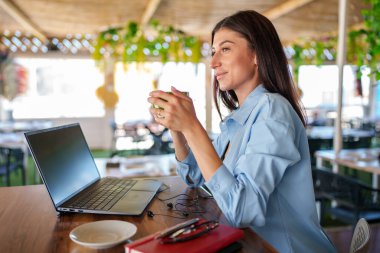 Profesyonel bir kadın laptopta yazarken kahvesini yudumluyor, öğle arasında kafeteryada dinleniyor.