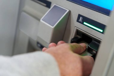 Otomatik veznedar makinesine kredi kartı sokup modern bankacılık ve finansal işlemlerin özünü yakalayan bir elin görüntüsünü kapat.