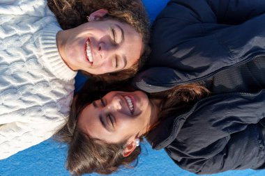 İki mutlu genç kadın mavi bir arka planda uzanıyorlar, rahatlama ve kahkahaların tadını çıkarıyorlar.