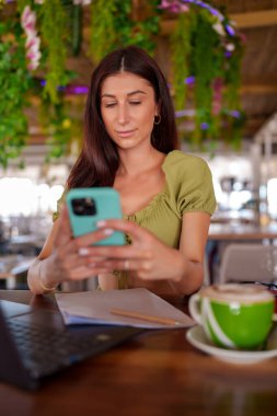 Tavandan sarkan bitkilerle modern bir iş yerinde cep telefonu kullanan genç bir iş kadını