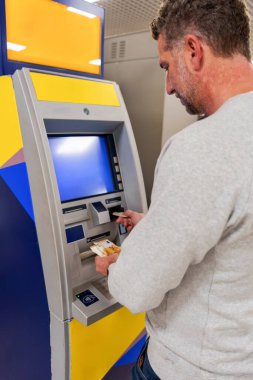 Otomatik veznedardan avro banknotlarını çeken bir adam, gündüz işlemleri sırasında fonlara hızlı ve uygun bir şekilde erişiyor