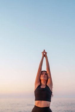 Yoga hocası gün batımında plajda esneme egzersizi yapıyor, sağlığını ve sağlıklı bir yaşam tarzını destekliyor.