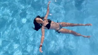 Genç dişi, mavi yüzme havuzu yüzeyinde zahmetsizce süzülüyor. Kaygısız yaz tatili rahatlığı ve huzurlu bir keyif yayıyor.