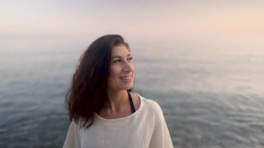 Huzurlu genç kadın özgürlüğünü yaşıyor, derin bir nefes alıyor altın gün batımı ışığı altında huzurlu okyanusun yanında dururken.