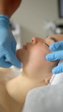 Profesyonel güzellik uzmanı mavi koruyucu eldiven giyer cilt bakımı sırasında genç Asyalı kadının yüzünü dikkatlice temizler kaplıca salonundaki beyaz havluya uzanır.