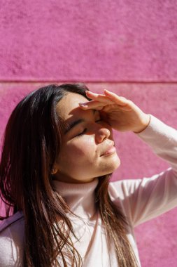 Manken gözlerini güneşten koruyor pembe bir duvarın önünde güneşli bir günün tadını çıkarıyor.